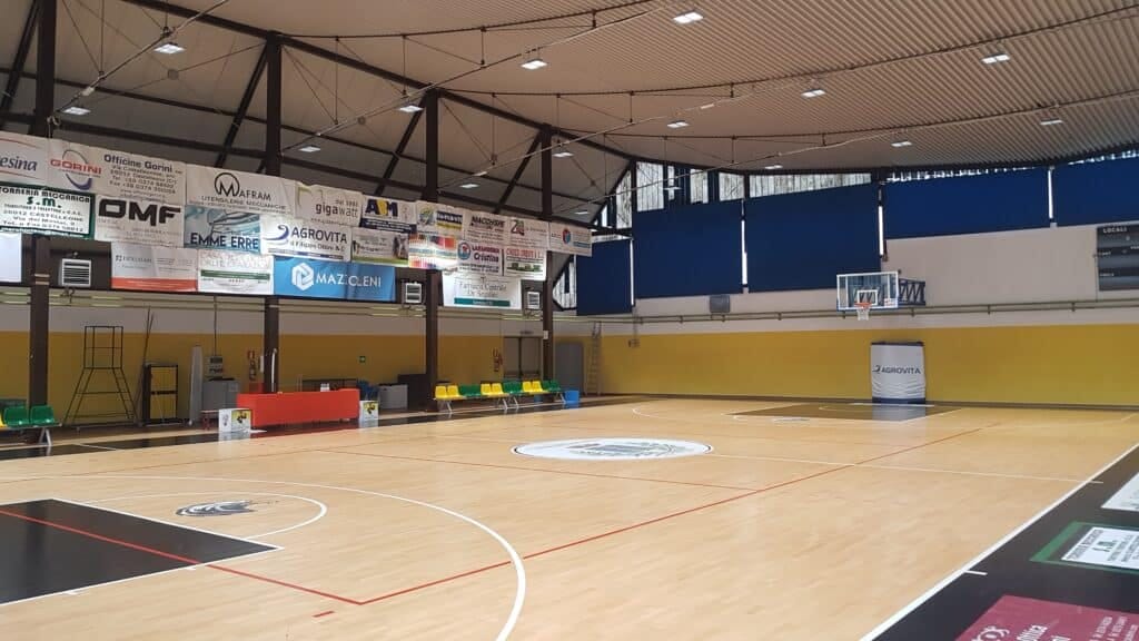 LED floodlights mounted on the steel roof trusses of an indoor sports hall, lighting the ceiling and court below